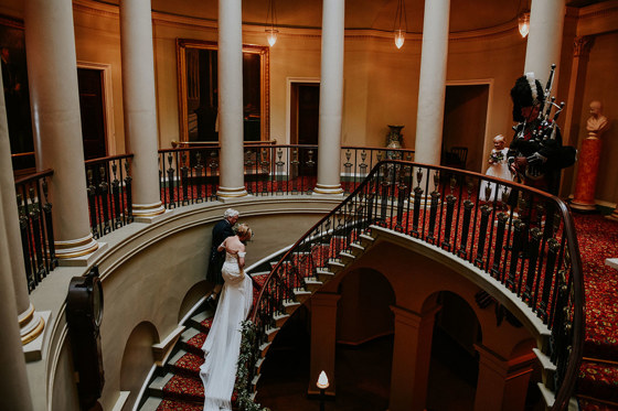 Newlyweds walk up the grand Oval Staircase with moody lighting and columns